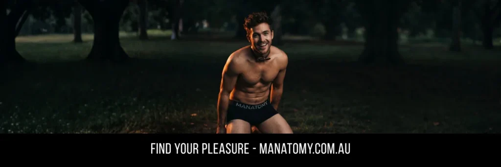 A grinning man in a collar kneeling on grass in a park at dusk, above a Find Your Pleasure banner.